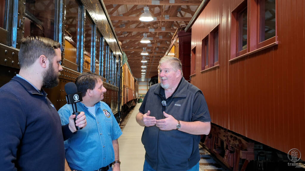 Three men standing next to a motorcar talking. Trains LIVE — Restoring Montana Western No. 31.