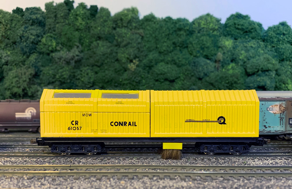 A boxy yellow maintenance-of-way car on a model railroad track