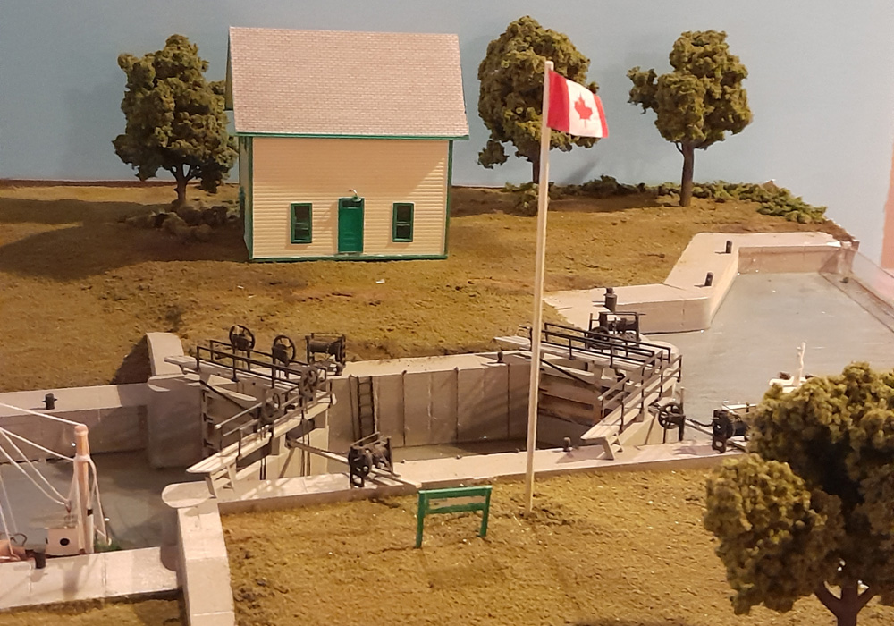 A model of a canal lock with a yellow wood building and a Canadian flag