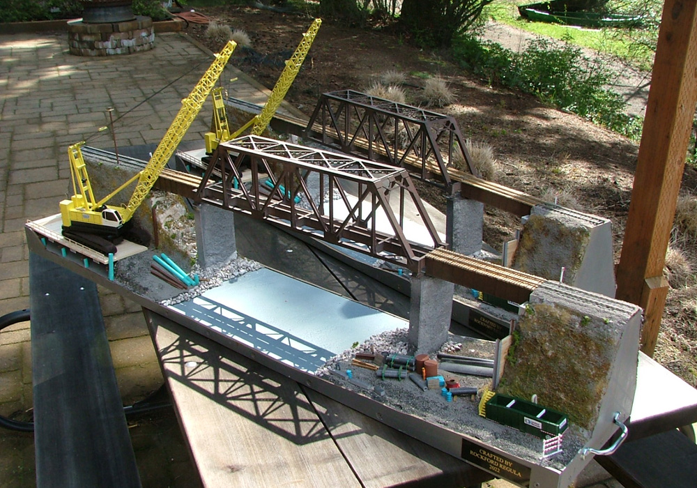 Two dioramas showing a steel bridge over a river under construction and a yellow crane