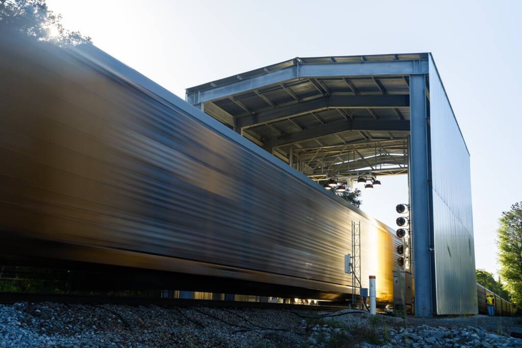 A train passes through a tall, gray, open-ended shed