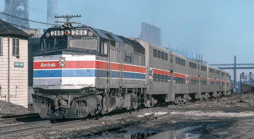 An amtrak train passes in front of industrial structures