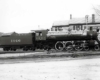 Steam locomotive resting aside wood-frame structure with advertising