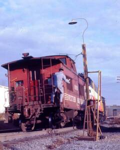 Man in blue on red caboose grabs paper from trackside structure from Preston Cook archive