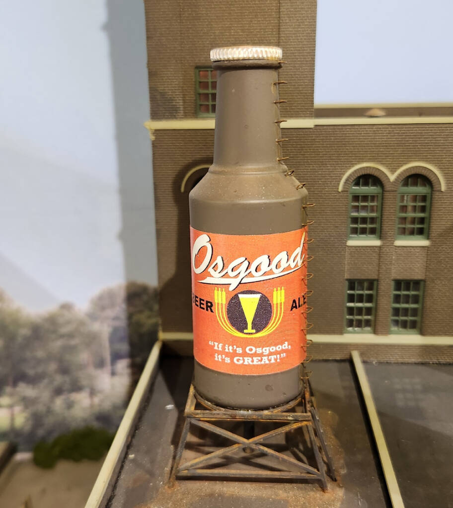 Color photo of small bottle painted brown on top of an HO scale building.
