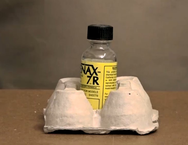 Color photo showing part of cardboard egg carton with a glue bottle in the middle.