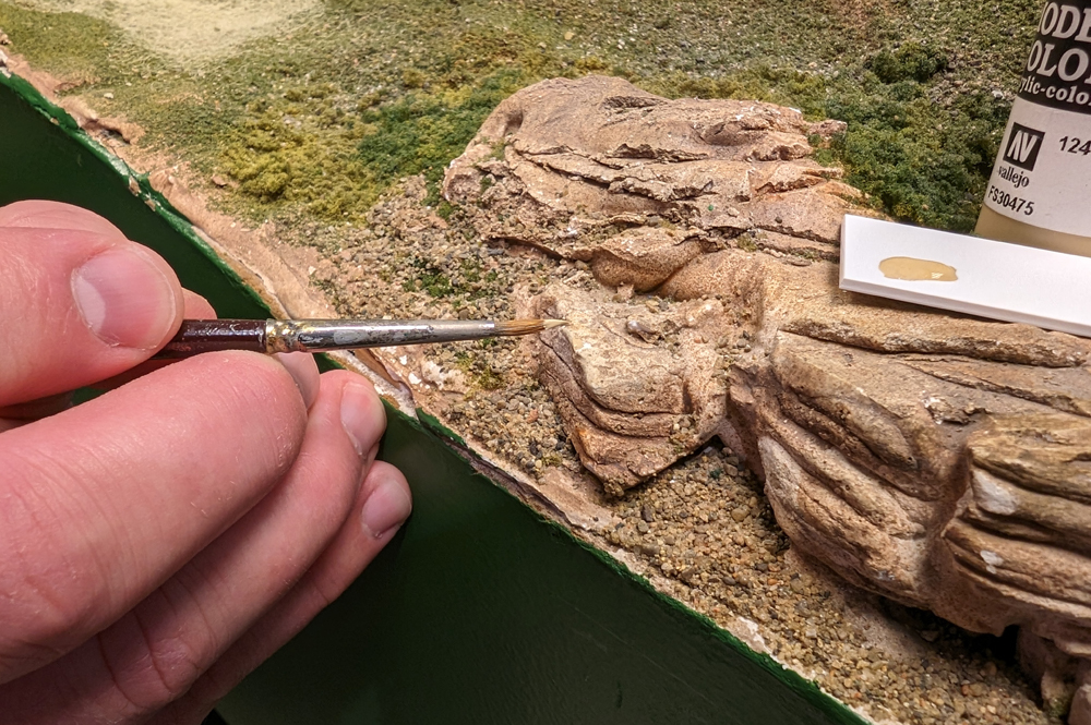 Color photo of hand holding paintbrush applying paint to rock castings. 