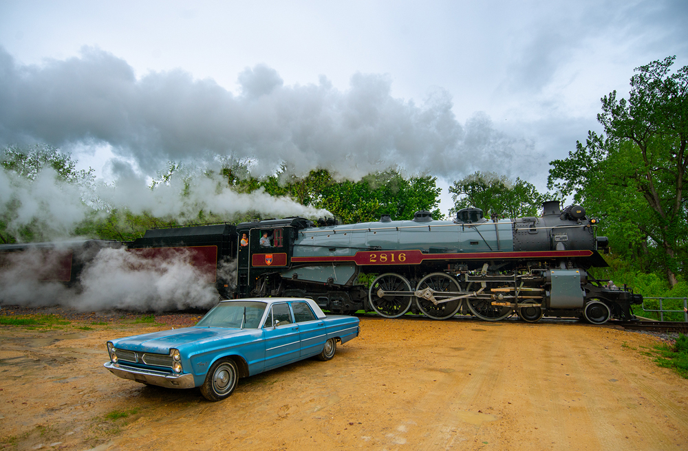 steam train behind old blue car