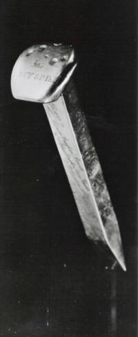 black and white photo of gold spike showing four small indentations on the head.