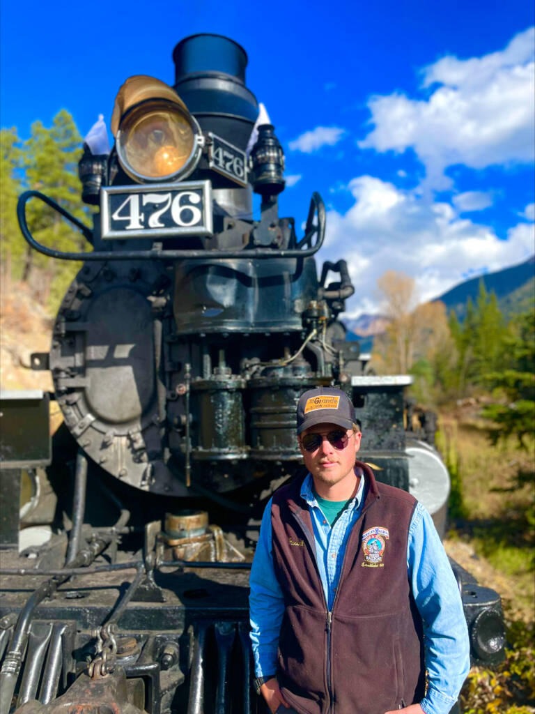 Young railroading employee posing in front of steam locomotive.