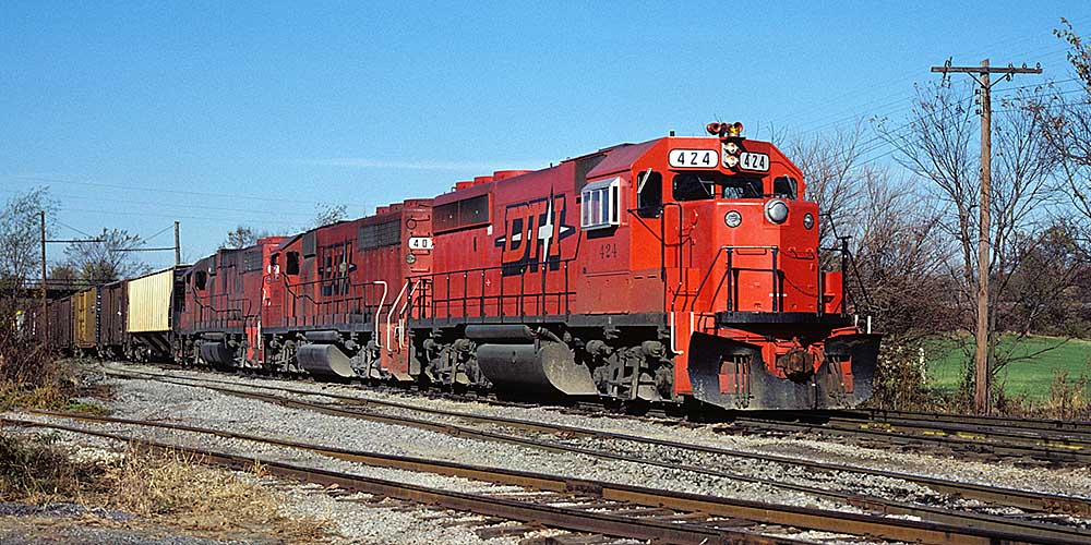 Orange-and-black diesel locomotives displaying traits of the Detroit, Toledo & Ironton with freight train under bridge