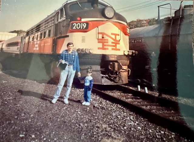 man holding boy’s hand next to diesel locomotive