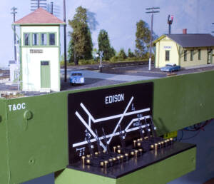 Black plastic models of Armstrong levers are mounted on the fascia of a model railroad below a model of an interlocking tower