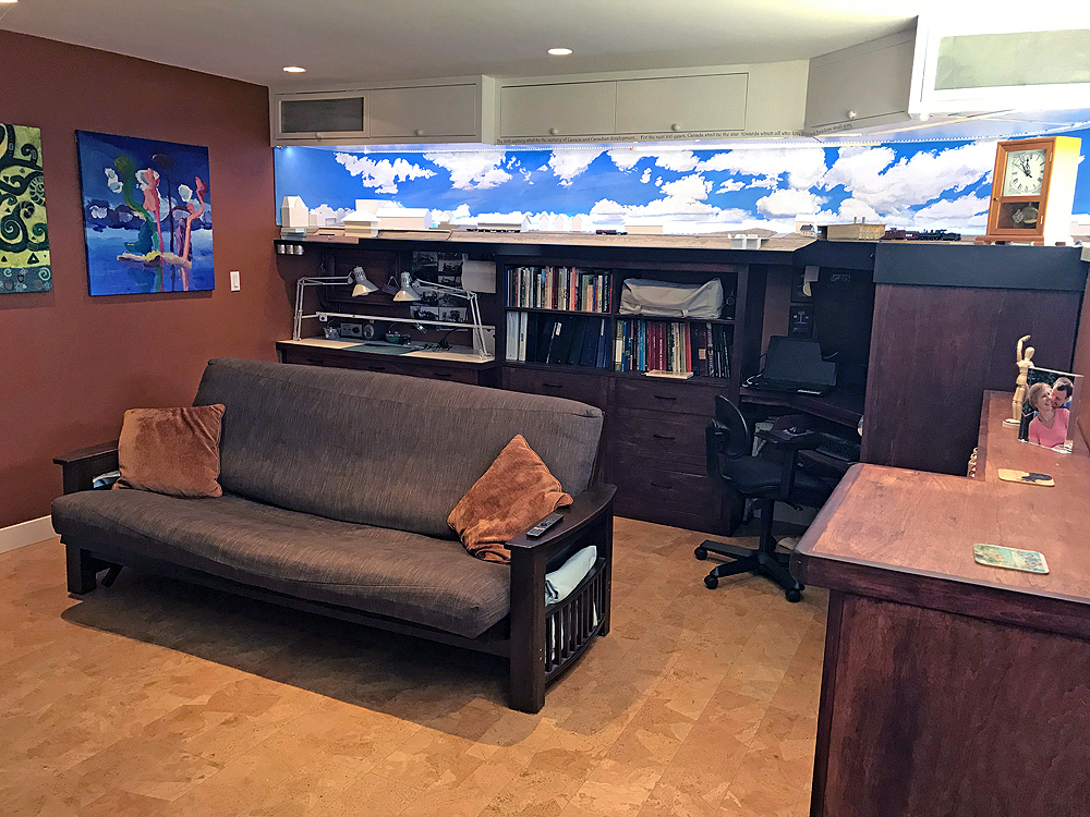 Color photo of basement room with model railroad, futon, and various work spaces and shelves.