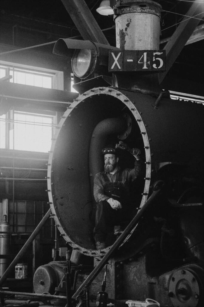 Black-and-white photo of young mechanic inside a steam locomotive