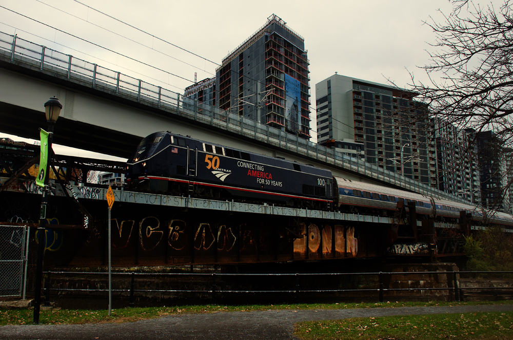 Dark blue Amtrak locomotive on passenger train with city skyline in background