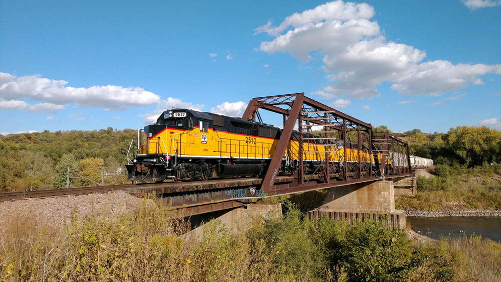 Yellow and black locomotives lead train crossing truss bridge over river