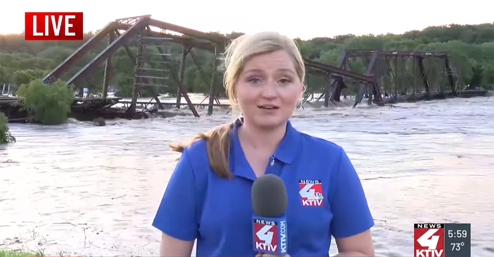 Woman standing in front of collapsed railroad bridge and flooding-swollen river