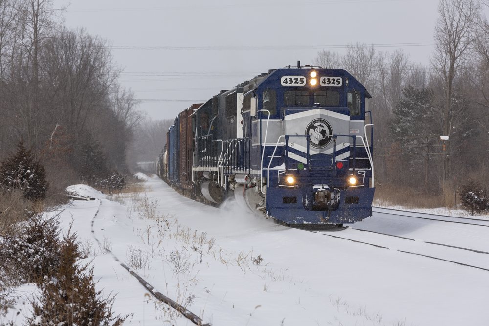Blue and gray locomotive leads freight train in snow