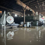 Two steam locomotives in roundhouse are surrounded by flood waters.