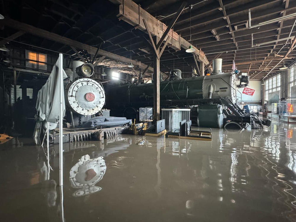 Two steam locomotives in roundhouse are surrounded by flood waters.