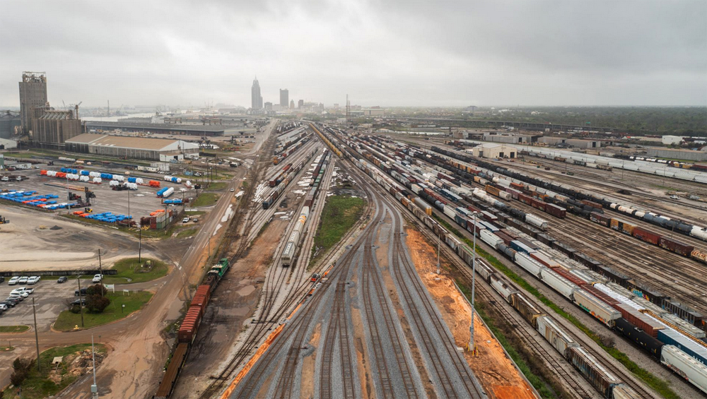 Aerial view of railyard under cloudy skies with city skyline in distance