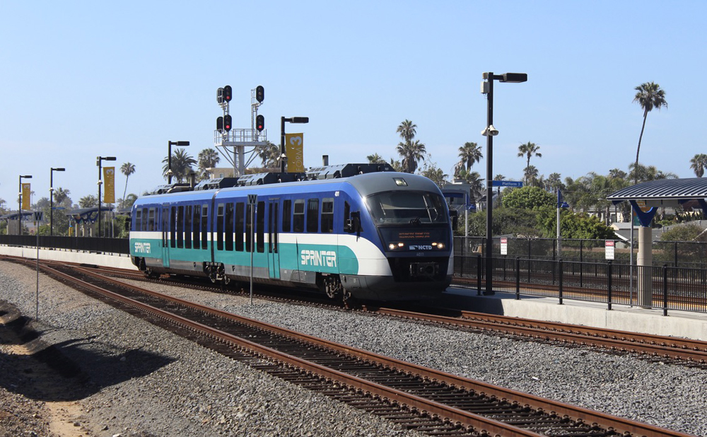 Blue, teal, and white diesel multiple-unit passenger train arrives at station platform