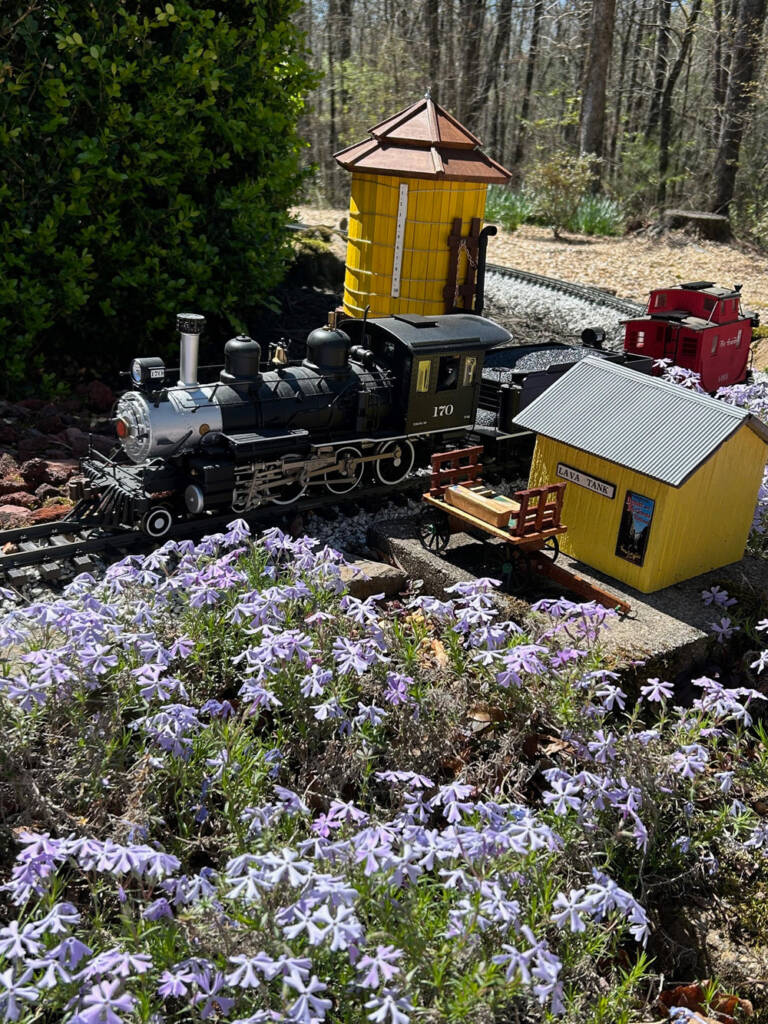 model steam engine next to yellow structure on garden railway