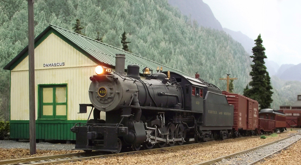 A steam-powered train stops at a small town station in the mountains