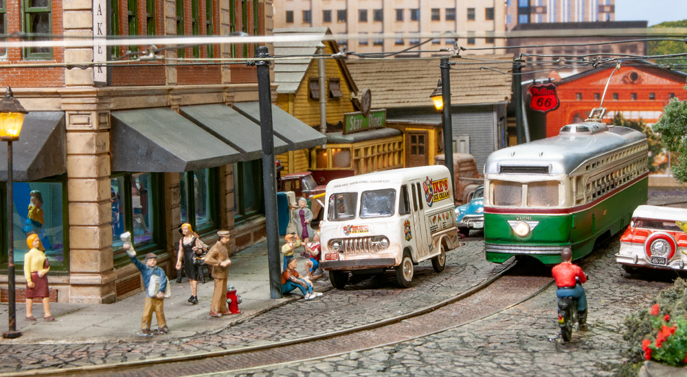 Pedestrians gather around an ice cream truck as a green trolley turns the corner