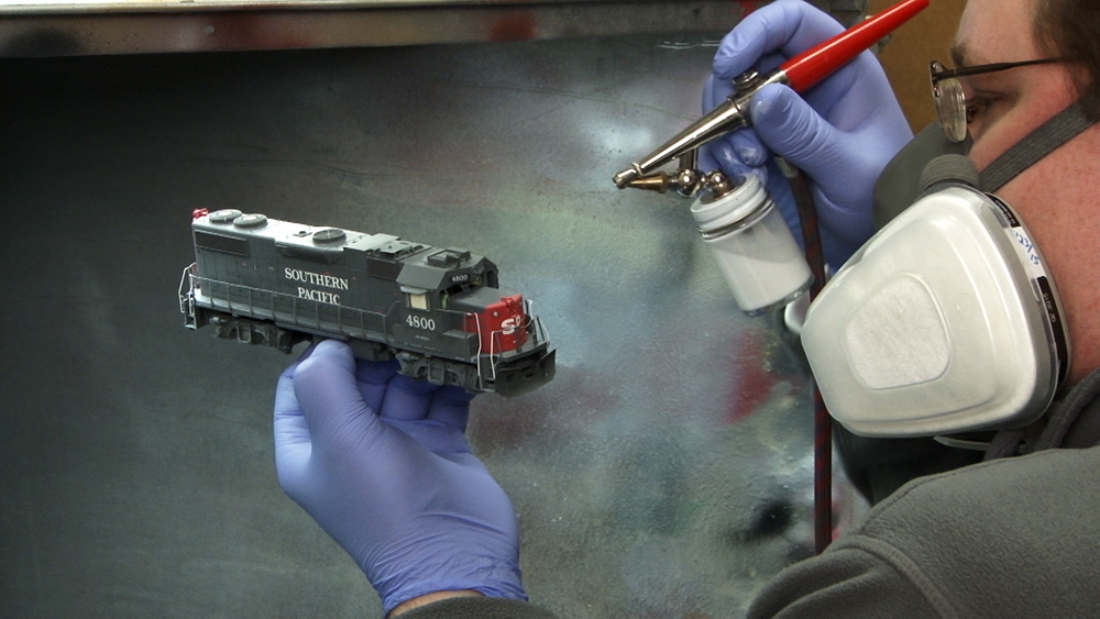 Photo of man painting HO scale diesel locomotive in spray booth.