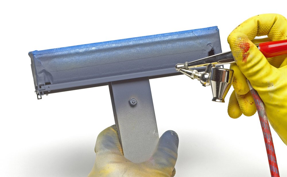 Color photo showing gloved hands holding an airbrush painting a freight car.