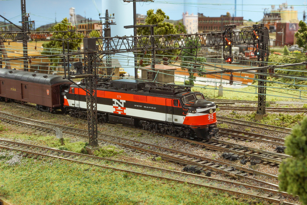 Orange, black, and white electric locomotive running under catenary. 