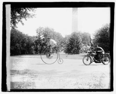 Large-wheeled velocipede being chased by a motorcycle.