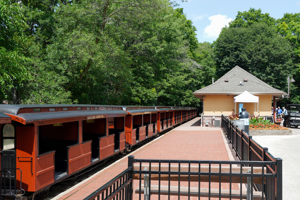 Wooden passenger cars sit in front of a passenger train station.