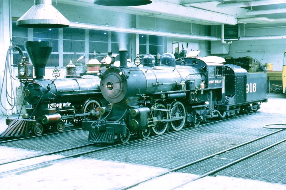 Two steam locomotives sit inside a shop.