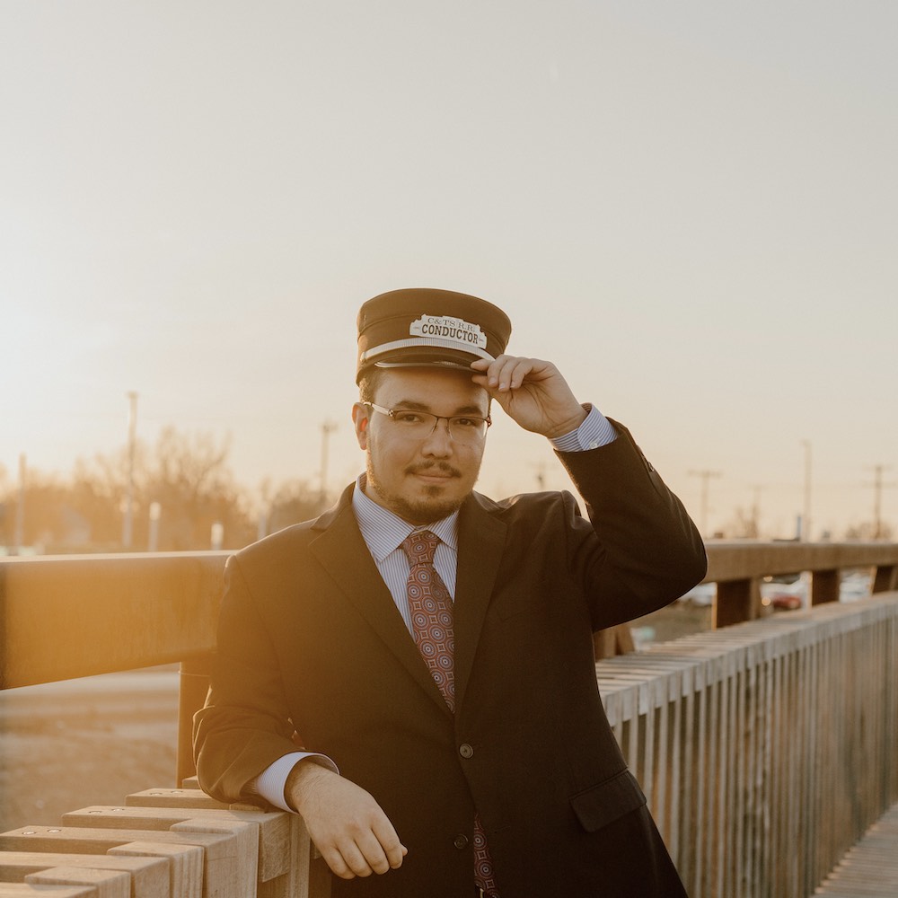 man in conductor uniform leaning on a wooden fence