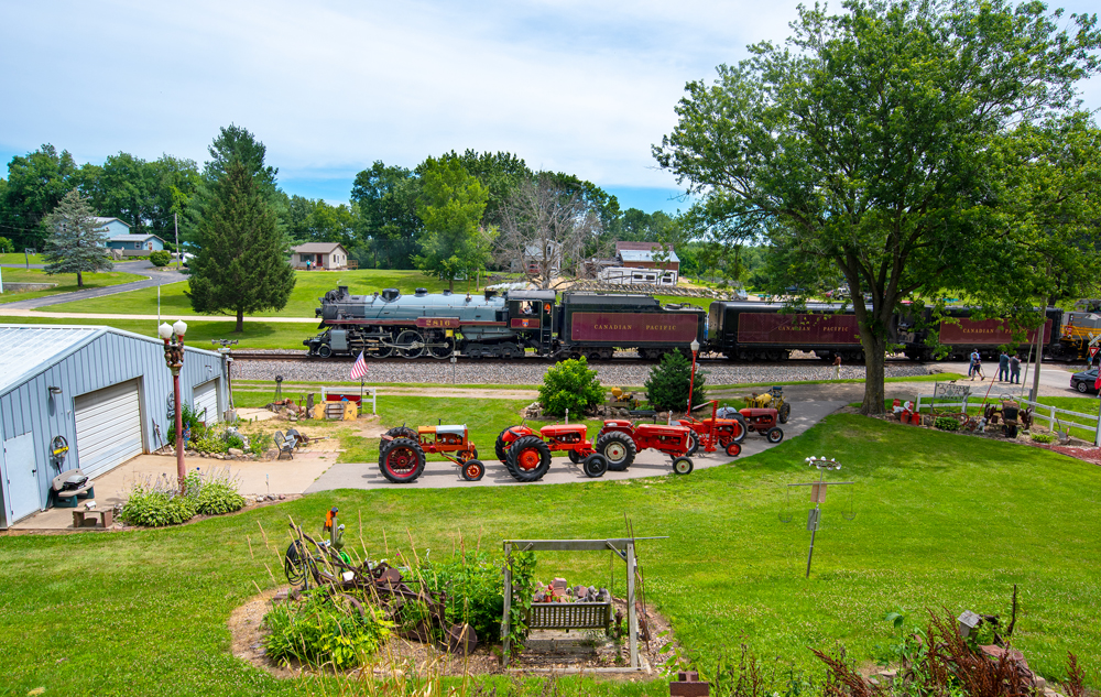 Steam locomotive passes line of tractors