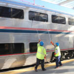 Two men with squeegees cleaning windows on bilevel passenger car.