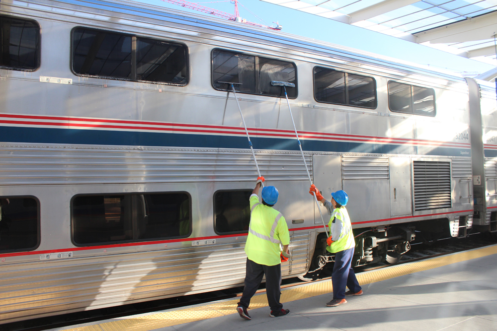 Two men with squeegees cleaning windows on bilevel passenger car.