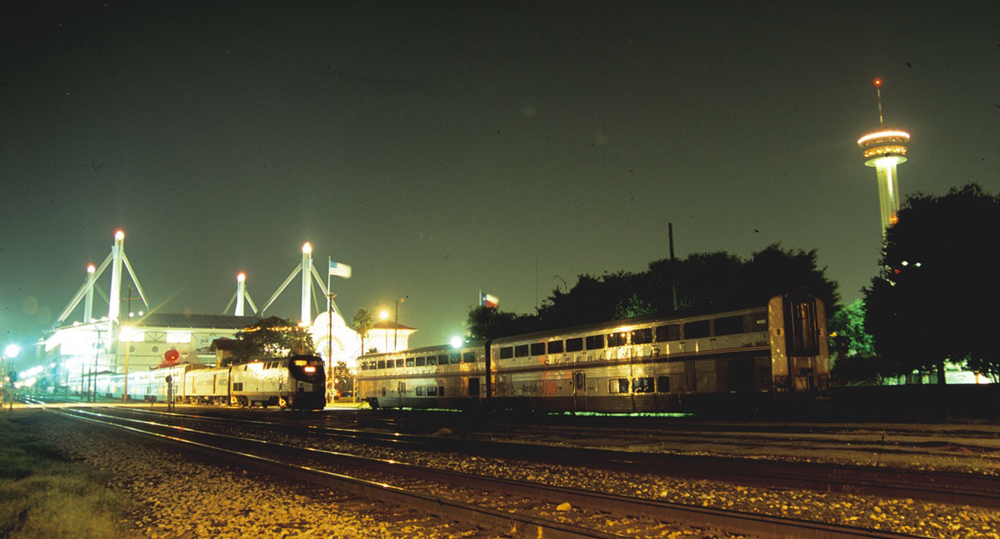 Two passenger cars sitting in darkness at station with train and San Antonio landmarks in the background