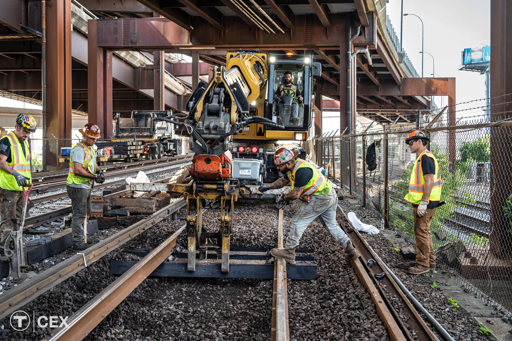 Equipment and men working on rail line under bridge