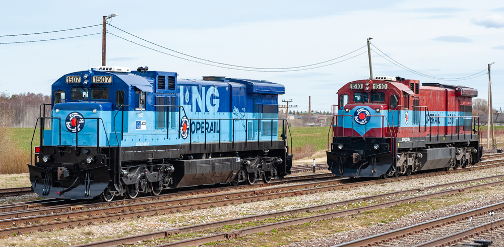 Two-tone blue GE locomotive next to maroon and blue locomotive.