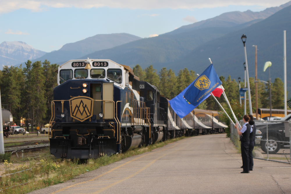 Passenger train greeted by individuals waving flags.