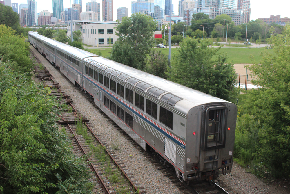 Rear of train of bilevel equipment with Chicago skyline in distance.