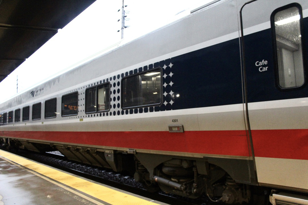 Close-up of silver passenger car with blue window stripe and red and white trim