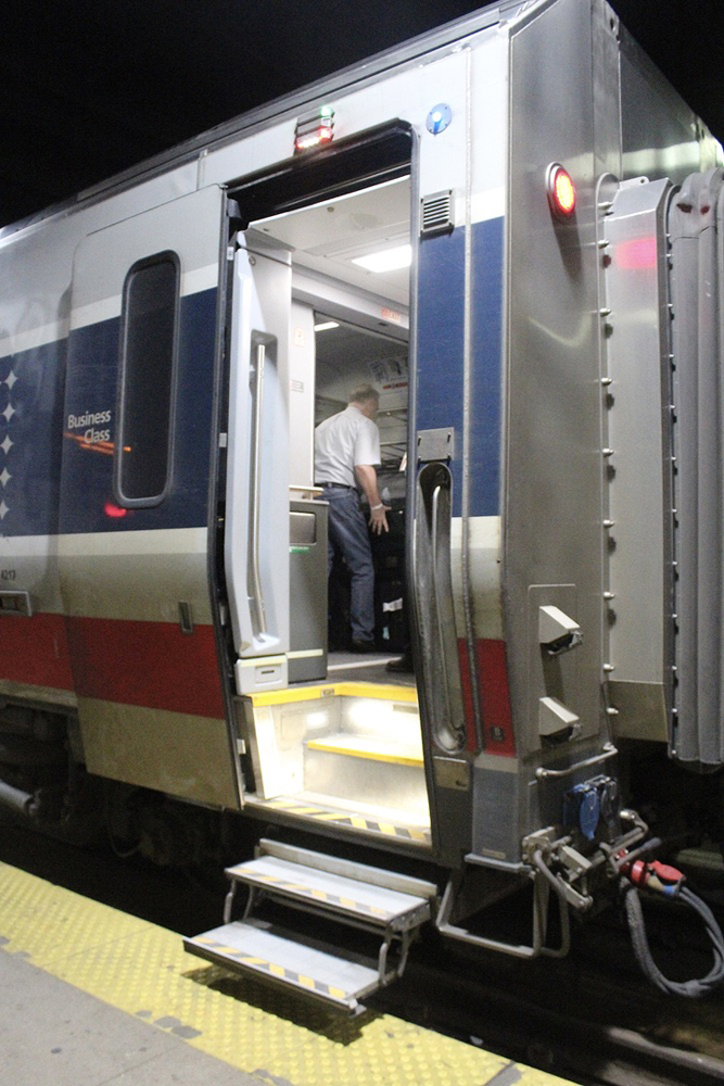 Open door on passenger car, with man visible storing suitcase inside