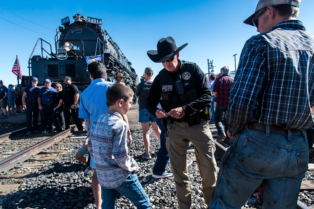 Man in black cowboy hat talks to boy with steam locomotive in background