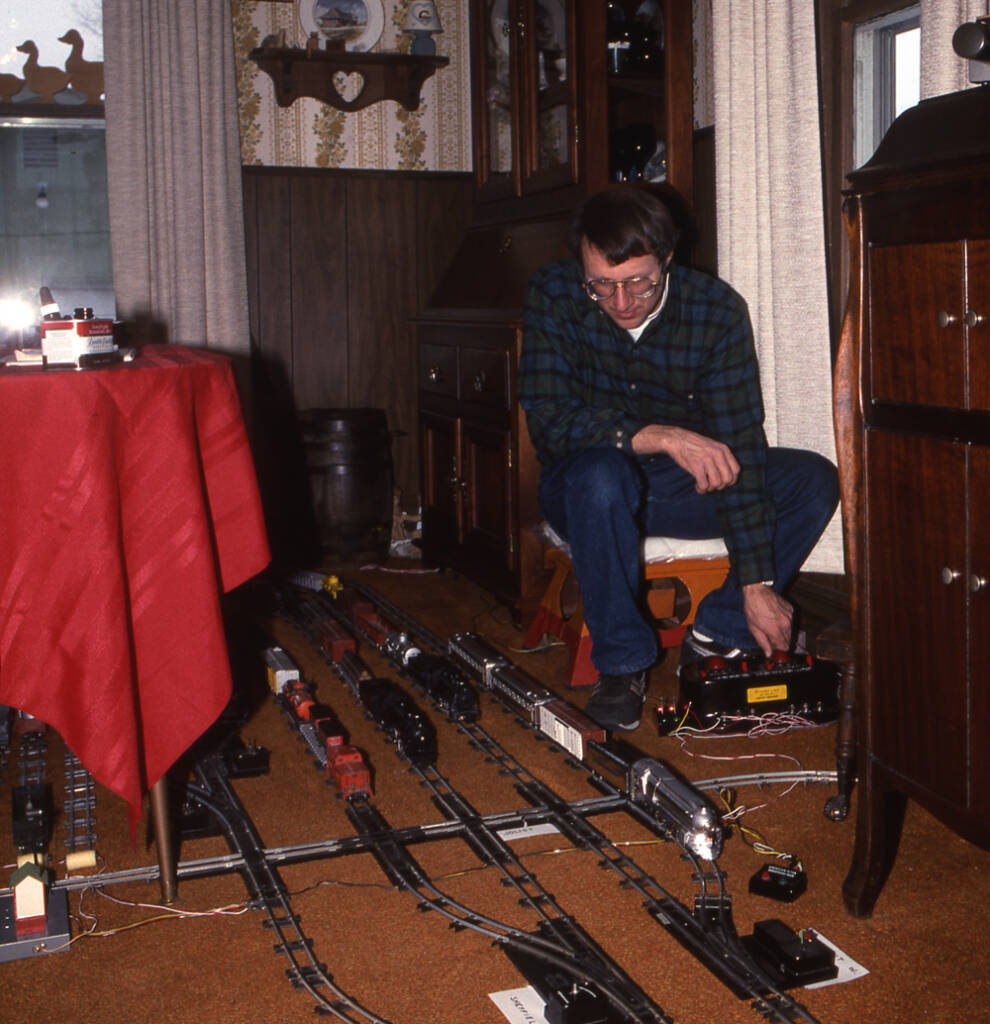 man on chair watches trains on floor; Celebrating “Flyer Fest”