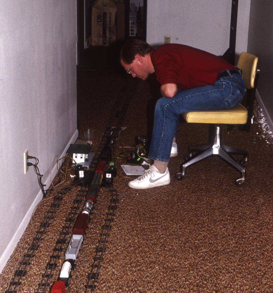 man on chair watches trains on floor